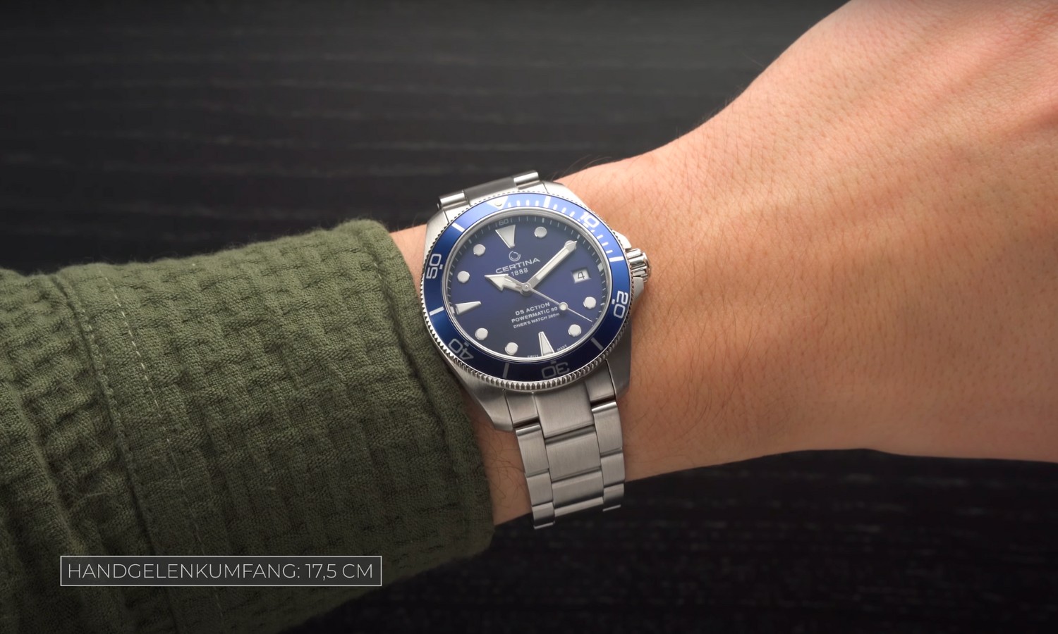 Die Certina DS Action Diver 38mm mit blauem Zifferblatt am Edelstahlarmband an einem Handgelenk mit grünem Ärmel getragen vor schwarzem Hintergrund