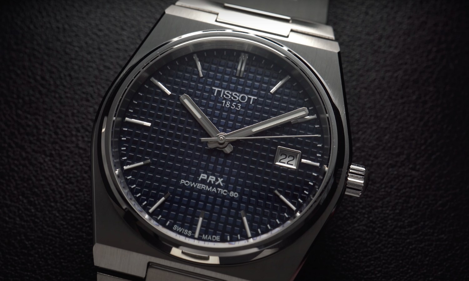 Nahaufnahme der Tissot PRX Powermatic 80 mit blauem Zifferblatt am Edelstahlarmband liegend vor schwarzem Hintergrund