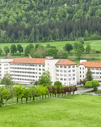 Farbaufnahme des Unternehmenssitzes von Longines in der Schweiz mit viel Grün und Wald im Vorder- und Hintergrund