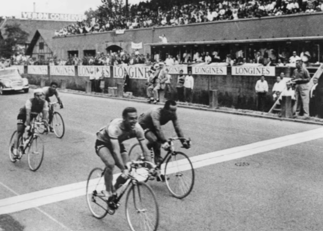 Schwarzweiß-Foto von Radfahrern, die vor Publikum die Ziellinie überfahren. Im Hintergrund ist der Longines-Schriftzug zu sehen