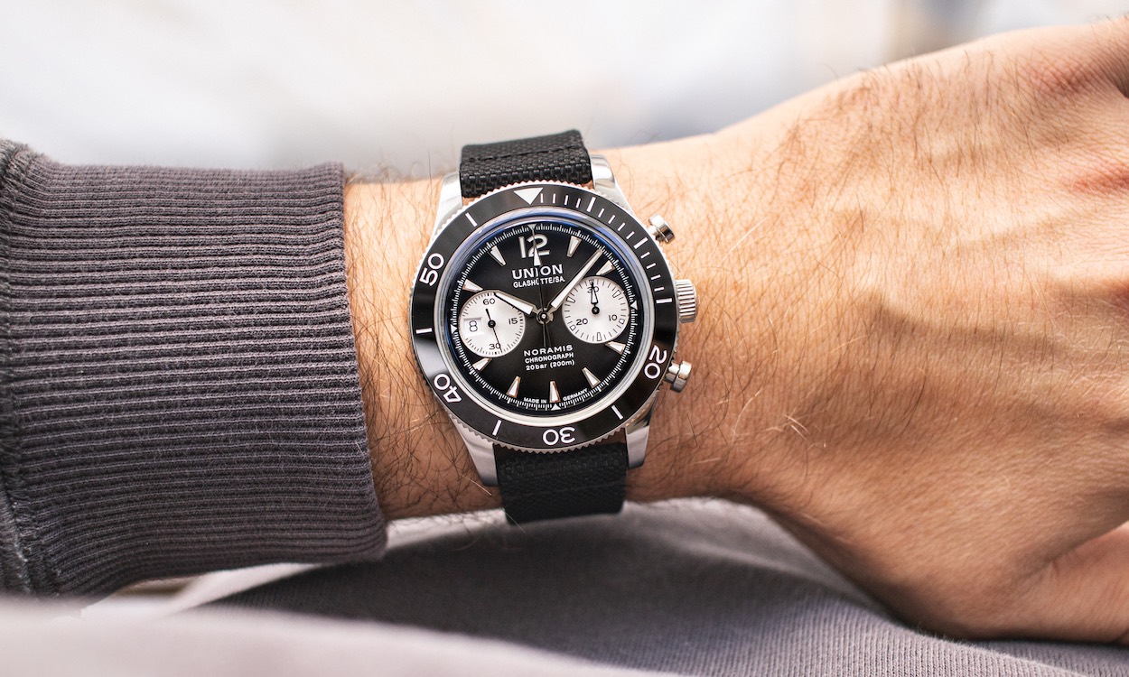 UNION Glashütte Noramis Chronograph Sport mit schwarzem Zifferblatt am schwarzen Textilarmband an einem Handgelenk mit Ärmel getragen vor hellem Hintergrund