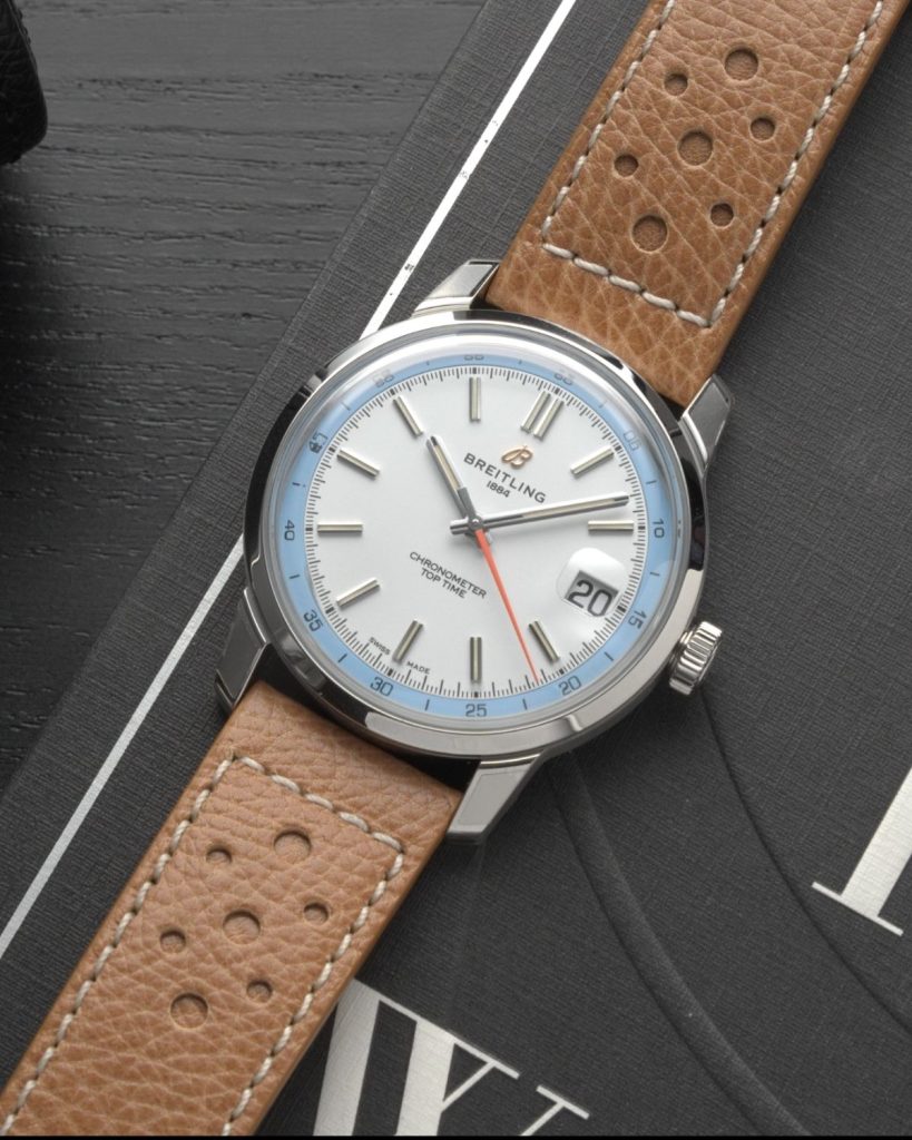 Die Breitling Top Time B31 mit weißem Zifferblatt am Lederarmband liegend vor schwarzem Hintergrund mit weißen Schriftzügen