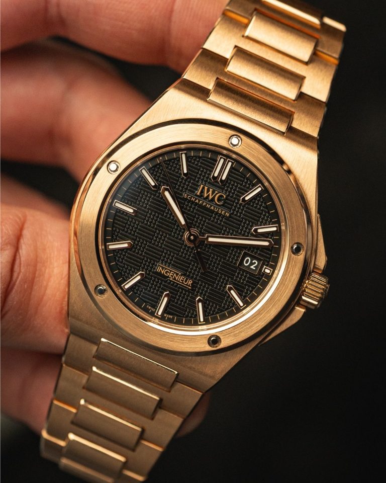IWC Ingenieur Automatic 40 mit schwarzem Zifferblatt und rotgoldenem Gehäuse und Armband in einer Hand gehalten vor schwarzem Hintergrund