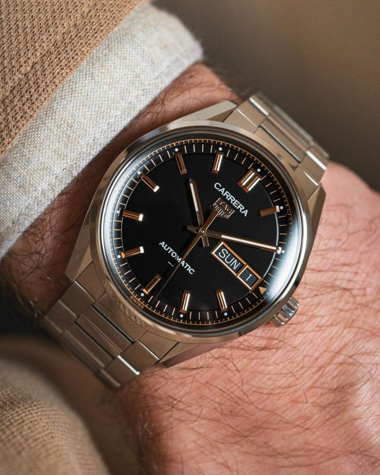 TAG Heuer Carrera Day-Date mit schwarzem Zifferblatt am Edelstahlarmband an einem Handgelenk mit beigem Ärmel getragen