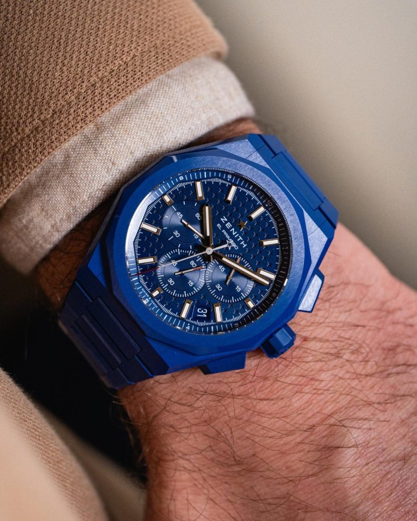 Zenith Defy Chronograph blaue Keramik mit blauem Zifferblatt am blauen Keramikarmband an einem Handgelenk mit beigem Ärmel getragen