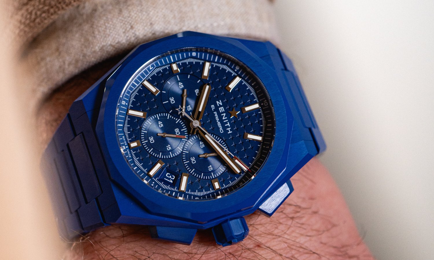 Zenith Defy Chronograph blaue Keramik mit blauem Zifferblatt am blauen Keramikarmband an einem Handgelenk mit beigem Ärmel getragen