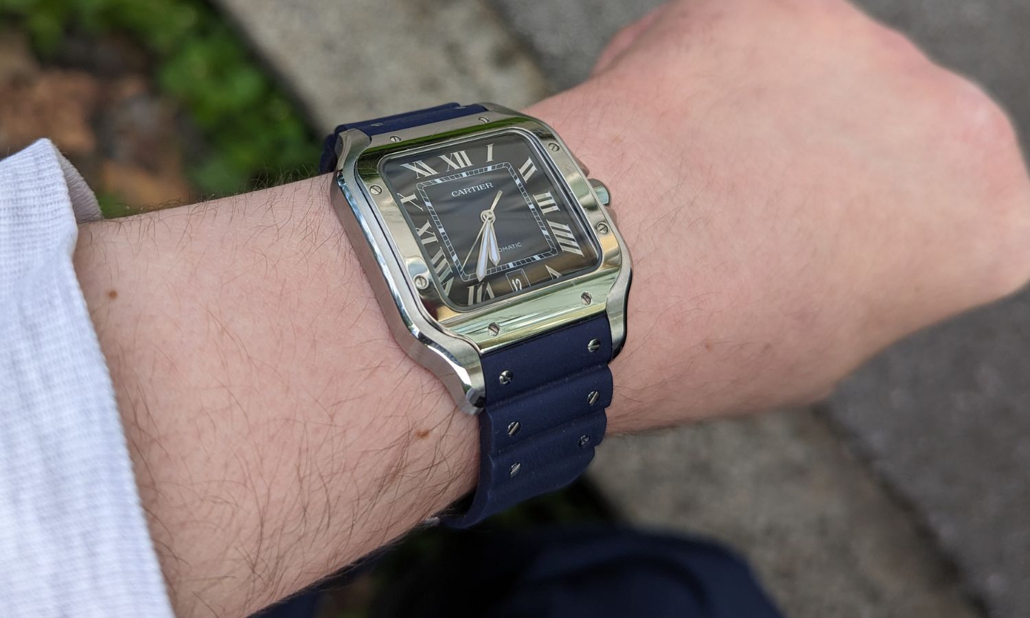 Blick auf die Cartier Santos de Cartier mit der Referenz WSSA0071 am blauen Kautschukband auf dem Handgelenk eines Mannes.