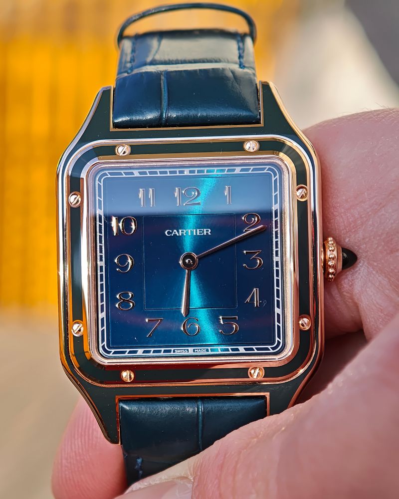 Nahaufnahme der Cartier Santos Dumont mit der Referenz WGSA0098 zwischen den Fingern eines Mannes.