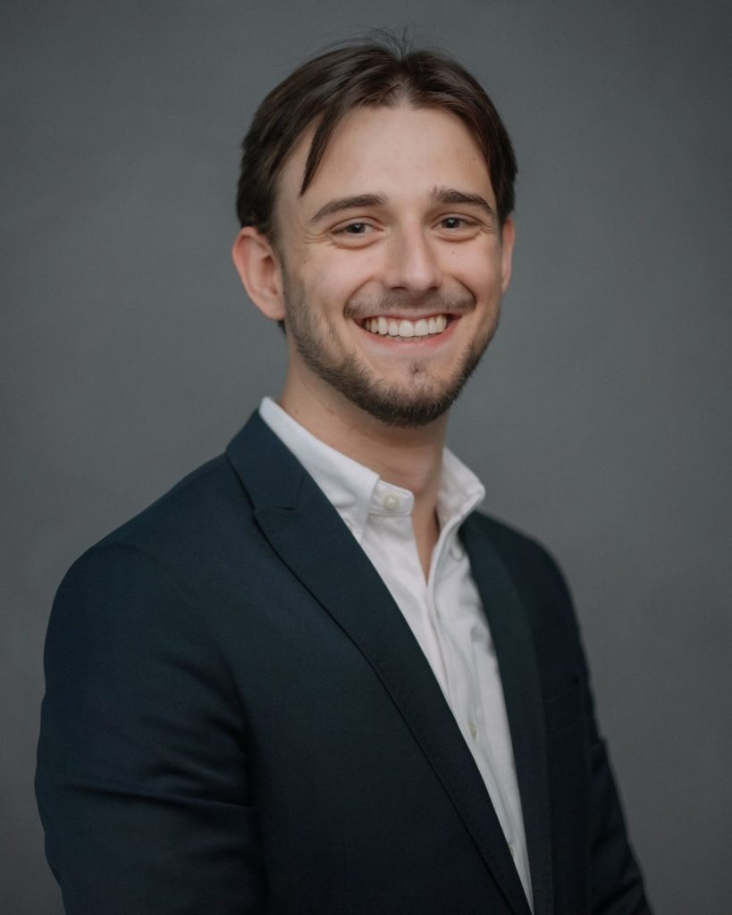 Johannes Karisch mit dunklem Jacket und weißem Hemd vor grauem Hintergrund