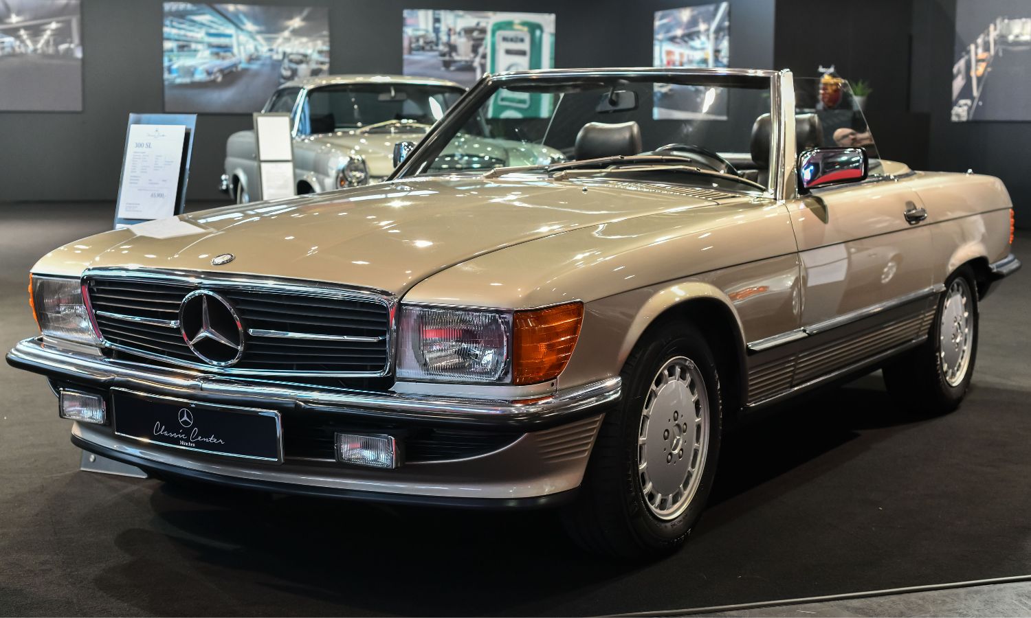 Blick auf ein beiges Cabrio von Mercedes Benz der Modellreihe R107 in einer Ausstellungshalle.