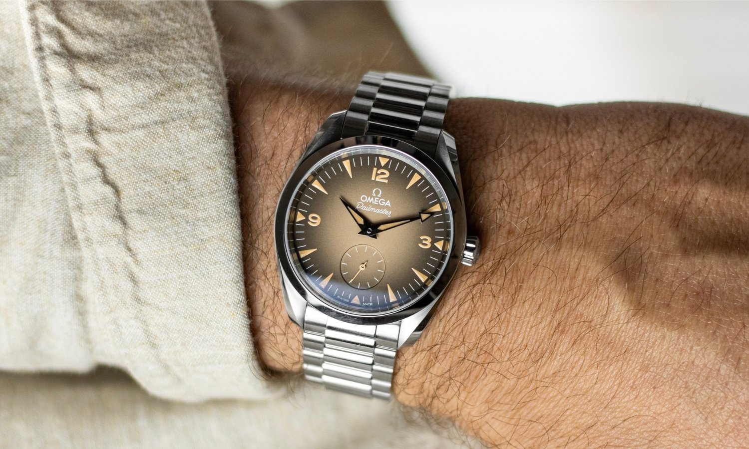 OMEGA Seamaster Railmaster Referenz: 235.10.38.20.13.001 mit beigem Zifferblatt am Edelstahlarmband an einem Handgelenk mit beigem Ärmel getragen