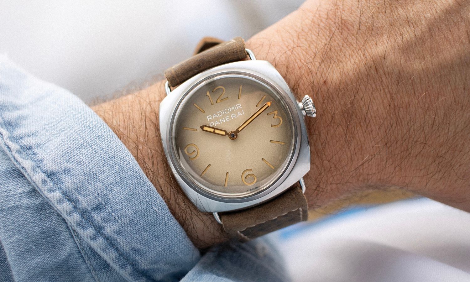 Panerai Radiomir Tre Giorni PAM01350 mit sandfarbenem Zifferblatt und hellbraunem Lederarmband abgebildet an einem Handgelenk mit hellblauem Ärmel vor weißem Hintergrund