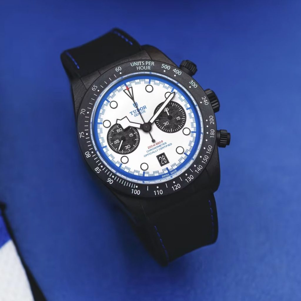 Blick von oben auf den TUDOR Black Bay Chrono Carbon 25, der auf auf einem blauen Boden liegt.