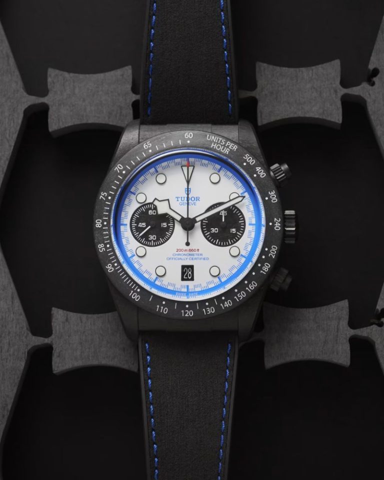 TUDOR Black Bay Chrono Carbon 25 mit weißem Zifferblatt am schwarzen Lederarmband liegend vor schwarz grauem Hintergrund