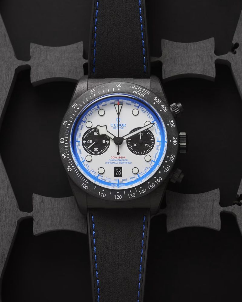 TUDOR Black Bay Chrono Carbon 25 mit weißem Zifferblatt am schwarzen Lederarmband liegend vor schwarz grauem Hintergrund