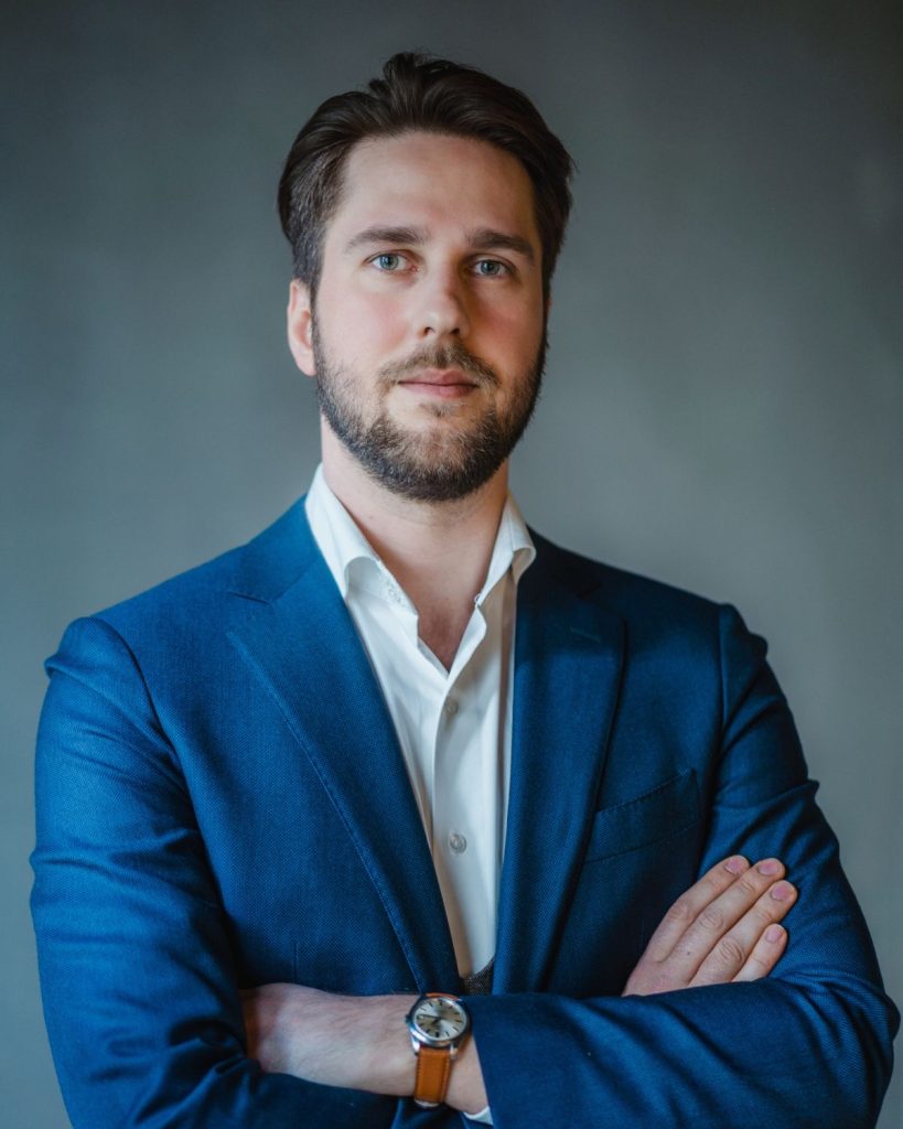 Thomas Dreblow mit blauem Jackett und weißem Hemd vor grauem Hintergrund