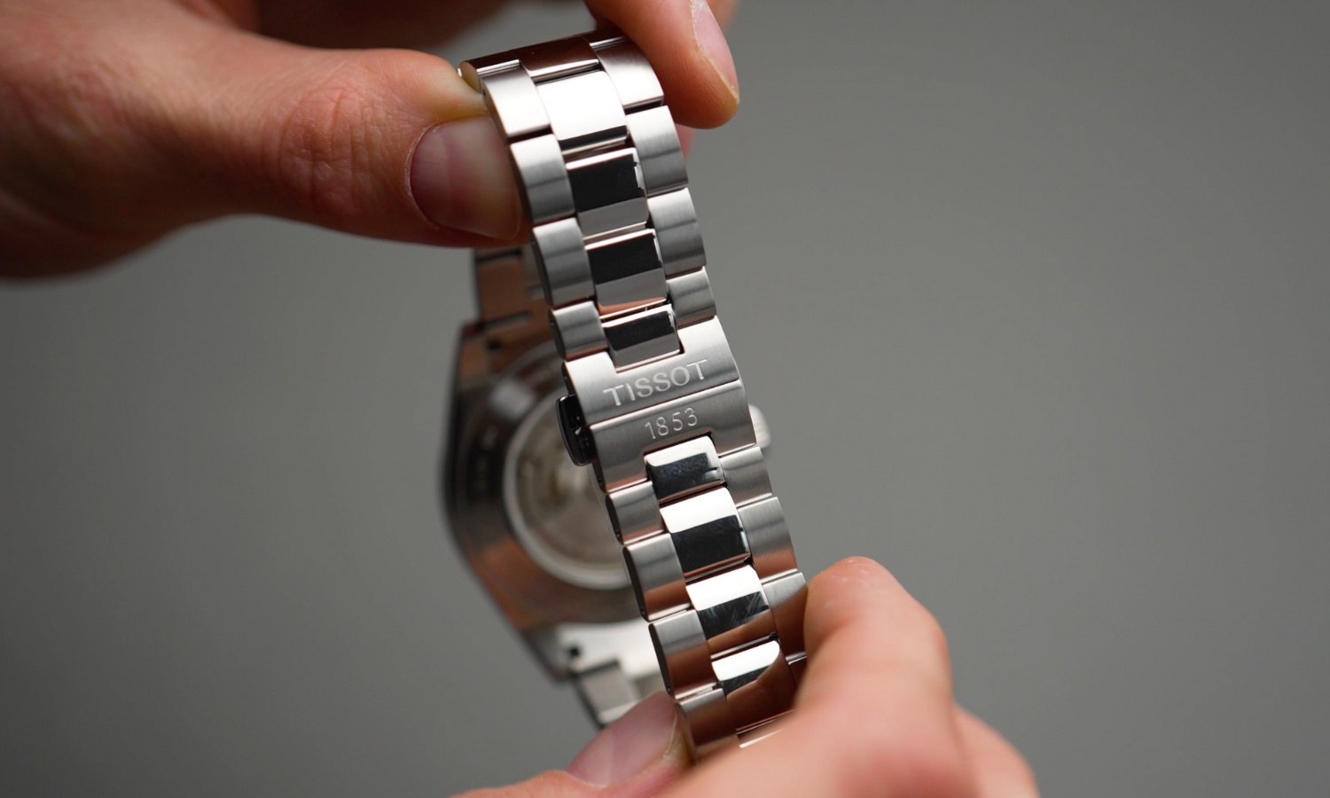 Das Edelstahlarmband und die Butterfly-Schließe der Tissot Gentleman Powermatic 80 in zwei Händen gehalten vor grauem Hintergrund