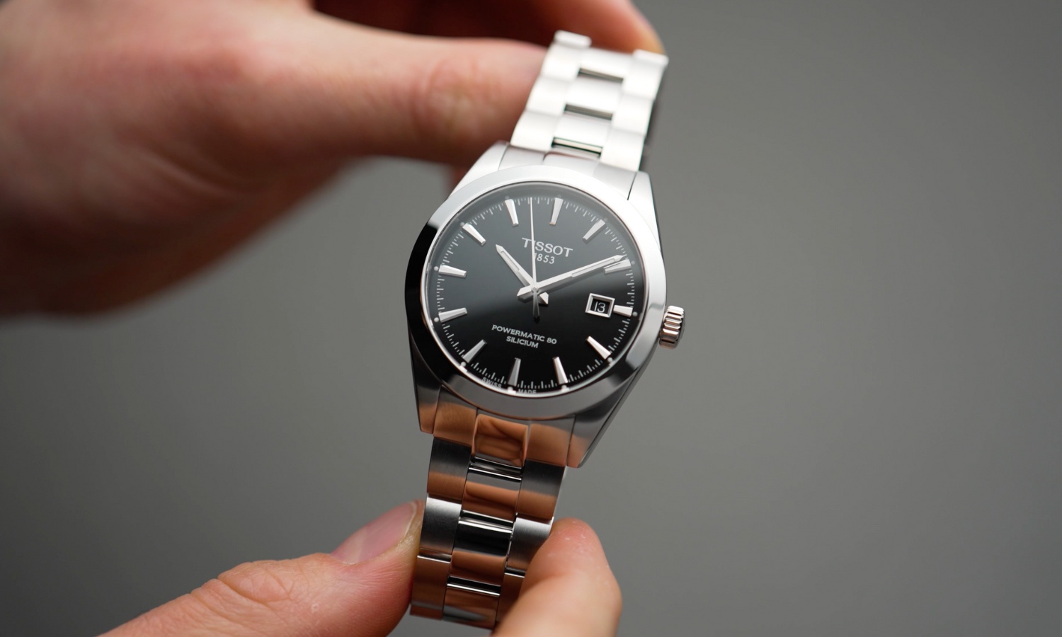 Tissot Gentleman Powermatic 80 Referenz: T127.407.11.051.00 mit schwarzem Zifferblatt am Edelstahlarmband in zwei Händen gehalten vor grauem Hintergrund