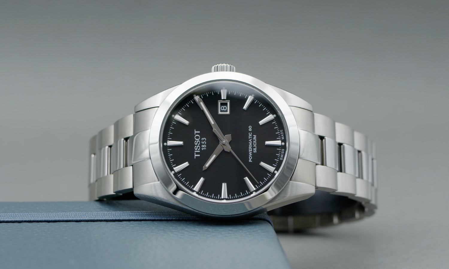 Tissot Gentleman Powermatic 80 Referenz: T127.407.11.051.00 mit schwarzem Zifferblatt am Edelstahlarmband auf der Seite liegend vor grauem Hintergrund
