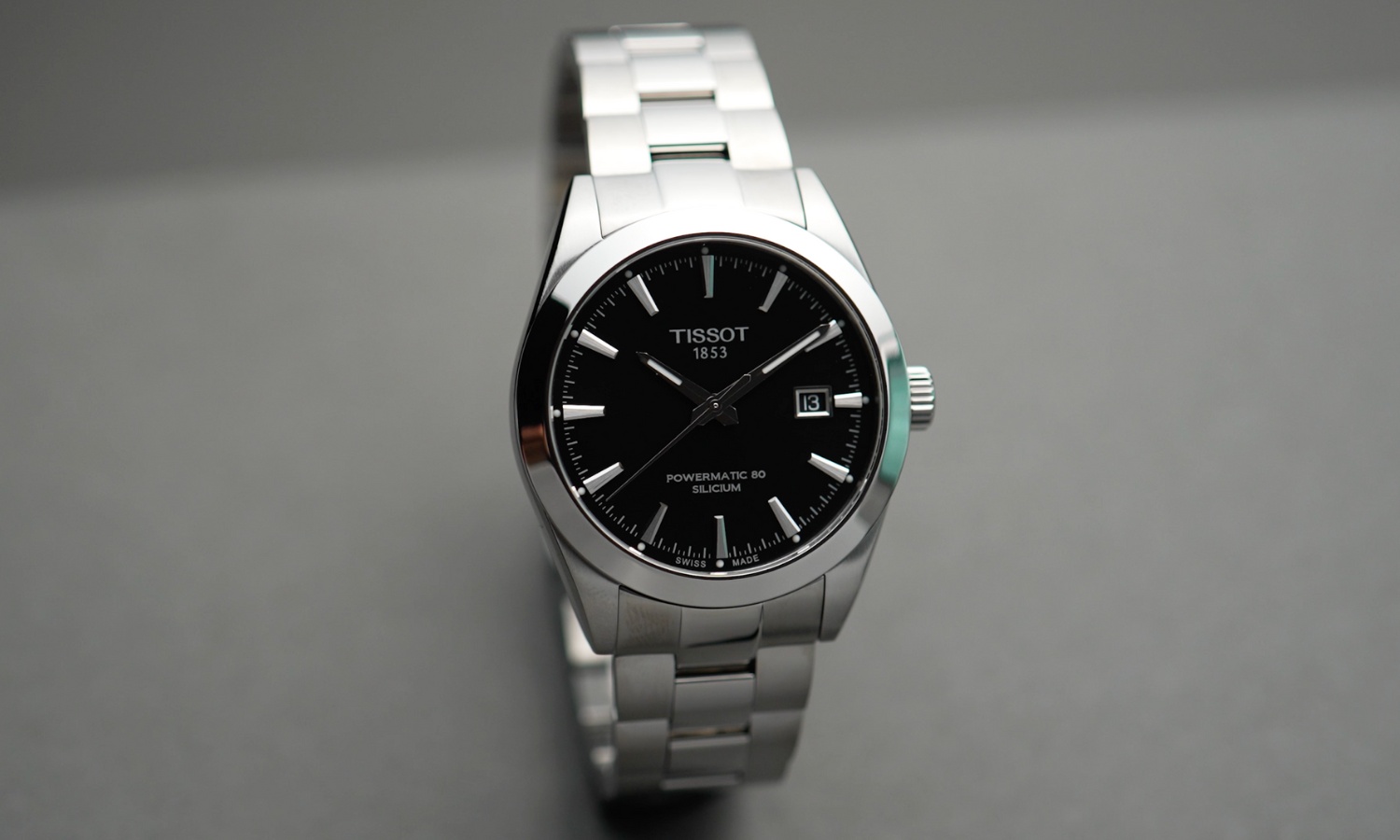 Tissot Gentleman Powermatic 80 Referenz: T127.407.11.051.00 mit schwarzem Zifferblatt am Edelstahlarmband stehend vor grauem Hintergrund
