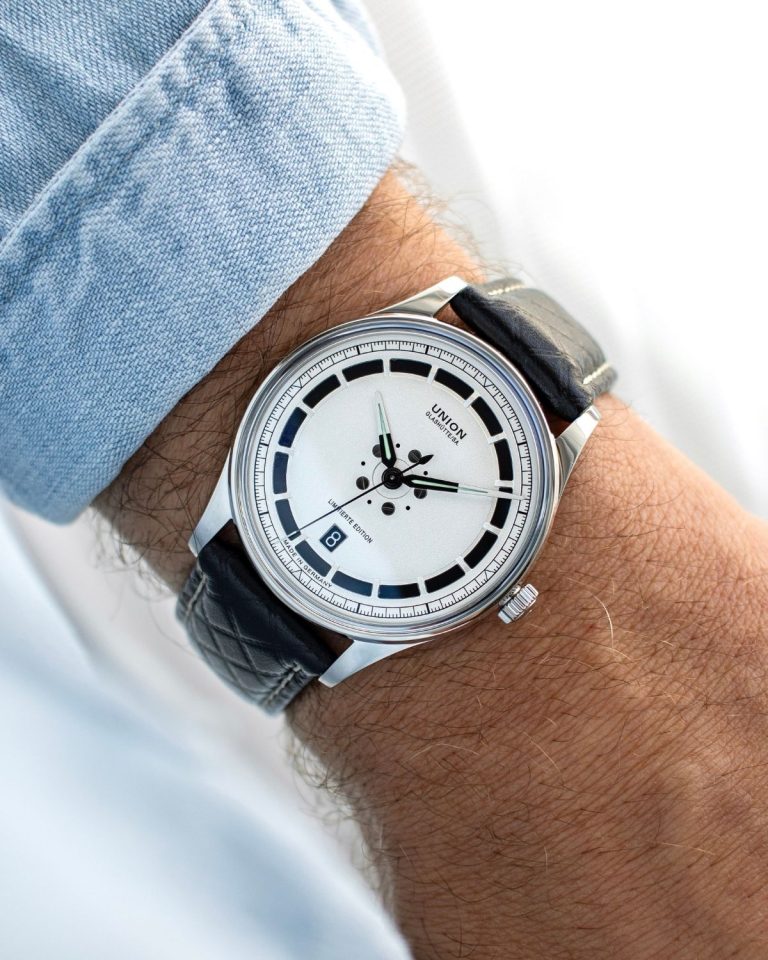 UNION Glashütte Noramis Datum Limitierte Edition Deutschland Klassik 2025 mit silbernem Zifferblatt am schwarzen Lederarmband an einem Handgelenk mit hellblauem Ärmel getragen vor hellem Hintergrund