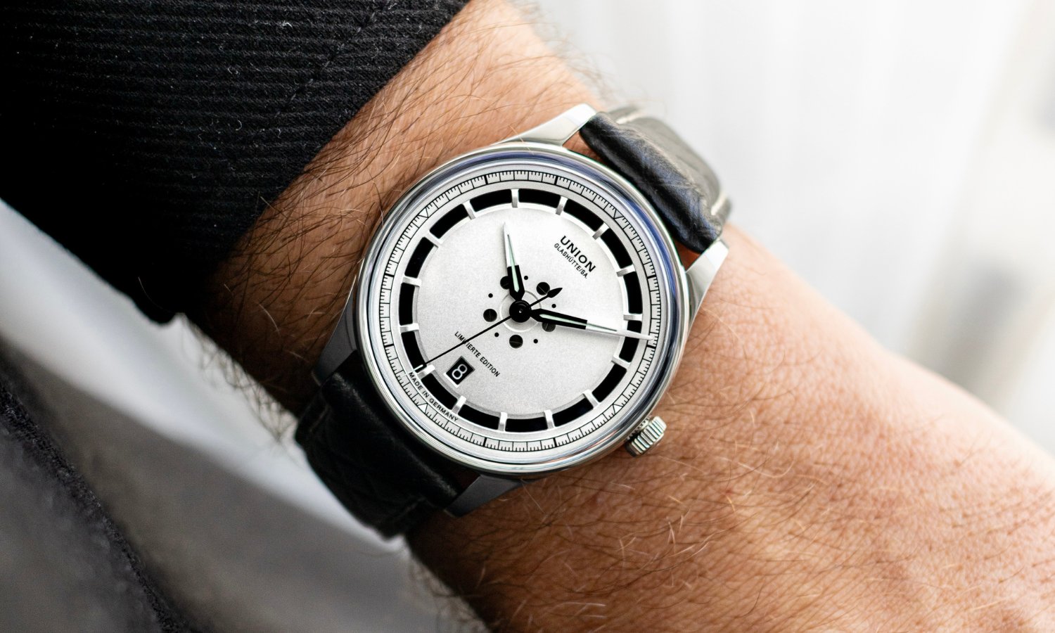 UNION Glashütte Noramis Datum Limitierte Edition Deutschland Klassik 2025 mit silbernem Zifferblatt am schwarzen Lederarmband an einem Handgelenk mit schwarzem Ärmel getragen vor hellem Hintergrund