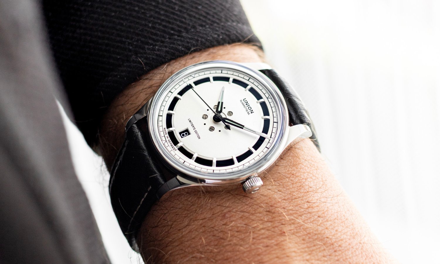 UNION Glashütte Noramis Datum Limitierte Edition Deutschland Klassik 2025 mit silbernem Zifferblatt am schwarzen Lederarmband an einem Handgelenk mit schwarzem Ärmel getragen vor hellem Hintergrund