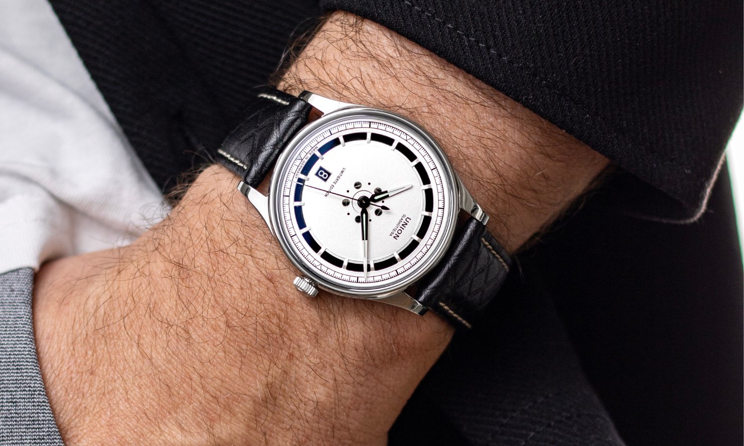 UNION Glashütte Noramis Datum Limitierte Edition Deutschland Klassik 2025 mit silbernem Zifferblatt am schwarzen Lederarmband an einem Handgelenk mit schwarzem Ärmel getragen vor schwarzem Hintergrund