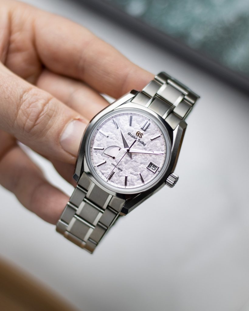 Grand Seiko Shunbun Referenz SBGA413 mit pinkem Zifferblatt am Edelstahlarmband in einer Hand gehalten vor hellem Hintergrund