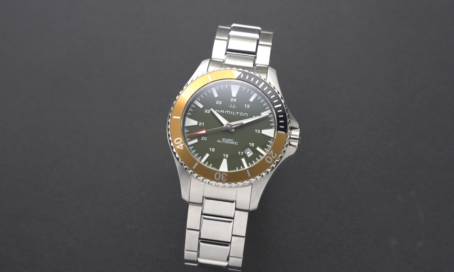 Hamilton Khaki Navy Scuba Auto Referenz: H82375161 mit grünem Zifferblatt am Edelstahlarmband stehend vor dunkelgrauem Hintergrund