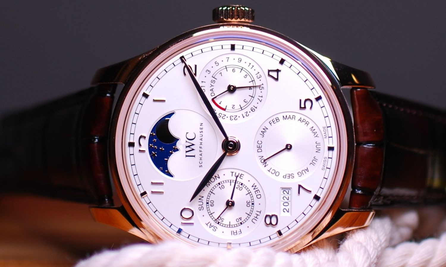 IWC Portugieser Perpetual Calendar 44 mit braunem Lederarmband und Roségoldgehäuse vor grauem Hintergrund mit einem Seil im Vordergrund liegend auf einem Holzuntergrund