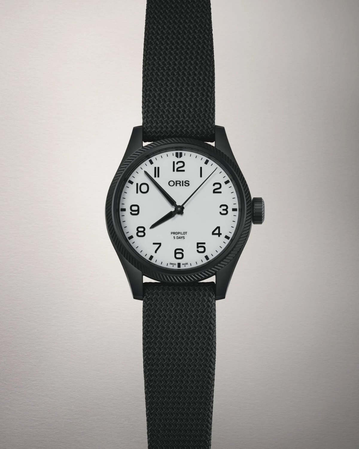 Frontalansicht auf die Oris ProPilot Hölstein Edition 2025 mit weißem Zifferblatt am schwarzen Textilarmband vor hellgrauem Hintergrund