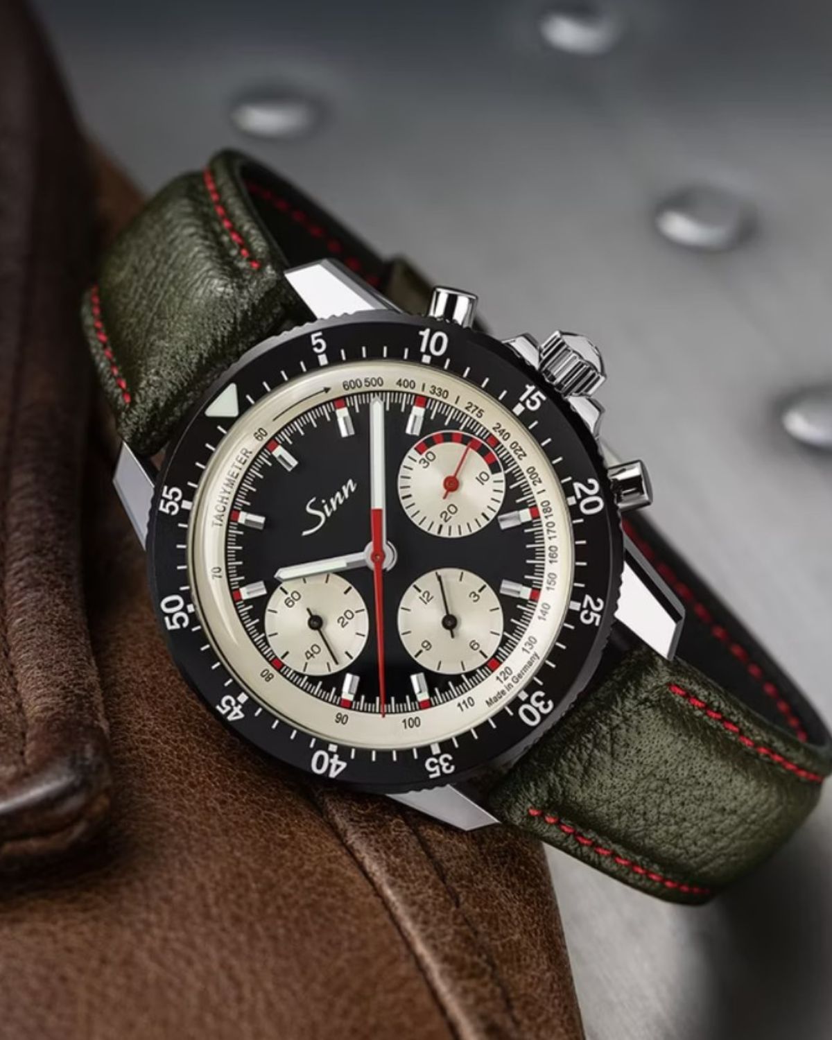 Sinn 103 ST Ty Hd Limitierte Edition mit schwarzem Zifferblatt und grünem Armbanfdf liegend auf einem Lederprodukt vor grauem Industrial-Hintergrund