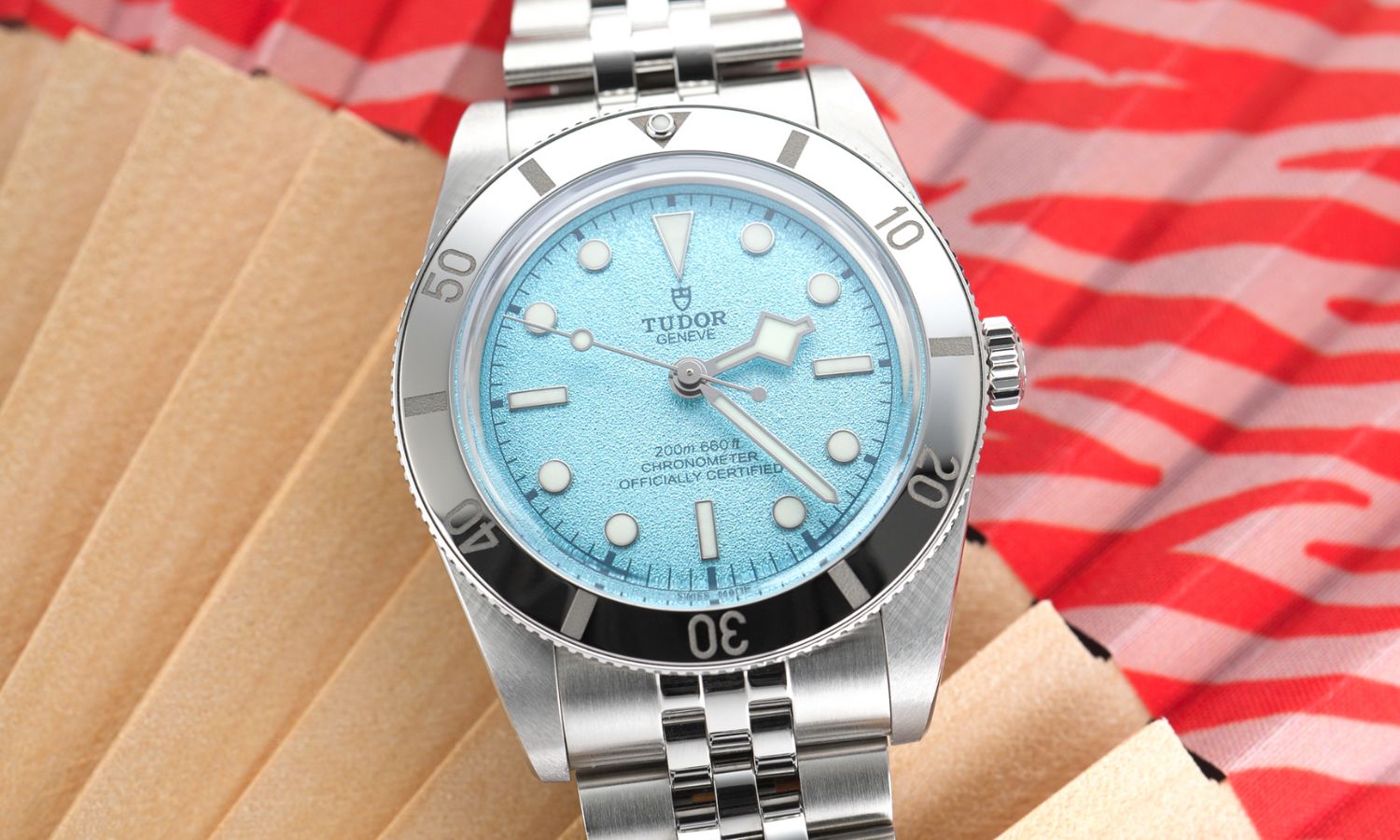 TUDOR Black Bay 54 Lagoon Blue Referenz: M79000-0001 mit hellblauem Zifferblatt am Edelstahlarmband liegend vor rotem Hintergrund