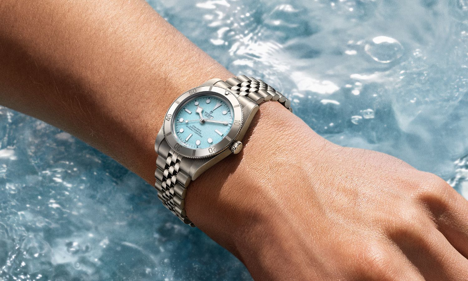 Seitlicher Blick auf die TUDOR Black Bay 54 Lagoon Blue mit der Referenz 79000 auf dem Handgelenk einer Frau, unter dem Arm ist blaues Meerwasser zu sehen.