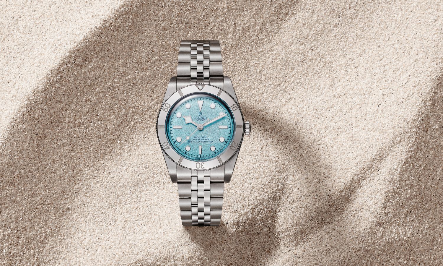 Blick auf die TUDOR Black Bay 54 Lagoon Blue mit der Referenz 79000 mit hellblauem Zifferblatt, die im Sand liegt.