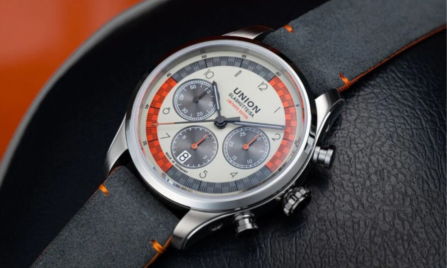 Union Glashütte Belisar Chronograph Silvretta Classic 2025 am schwarzen Lederarmband mit orangenen Zierelementen liegend auf einem schwarzen und strukturierten Untergrund
