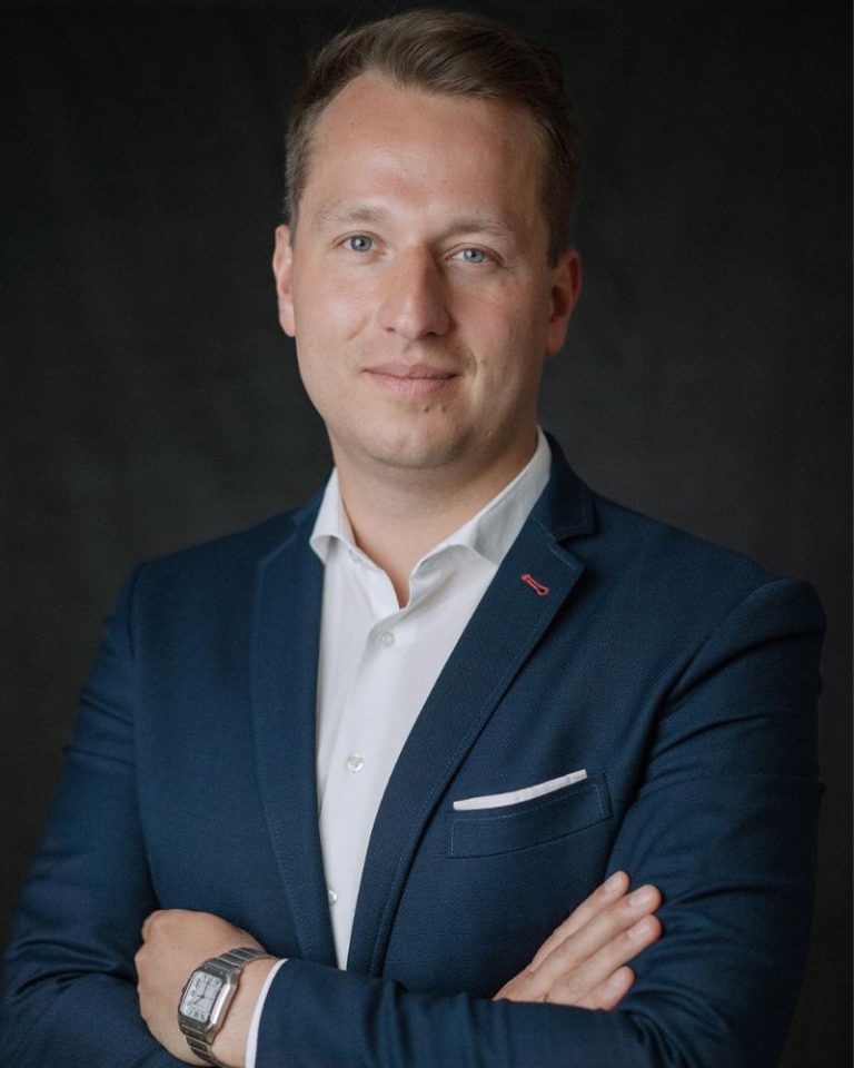 Porträtfoto von ALTHERR-Geschäftsführer Aleksej Dreiling, der einen blauen Anzug und eine Cartier Santos am Handgelenk trägt.