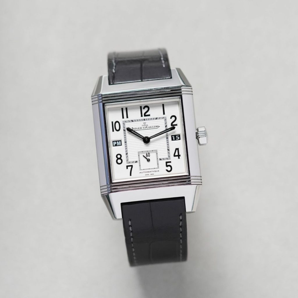 Jaeger-LeCoultre Reverso Squadra Hometime Referenz Q7008420 mit silbernem Zifferblatt am schwarzen Lederarmband stehend vor hellgrauem Hintergrund