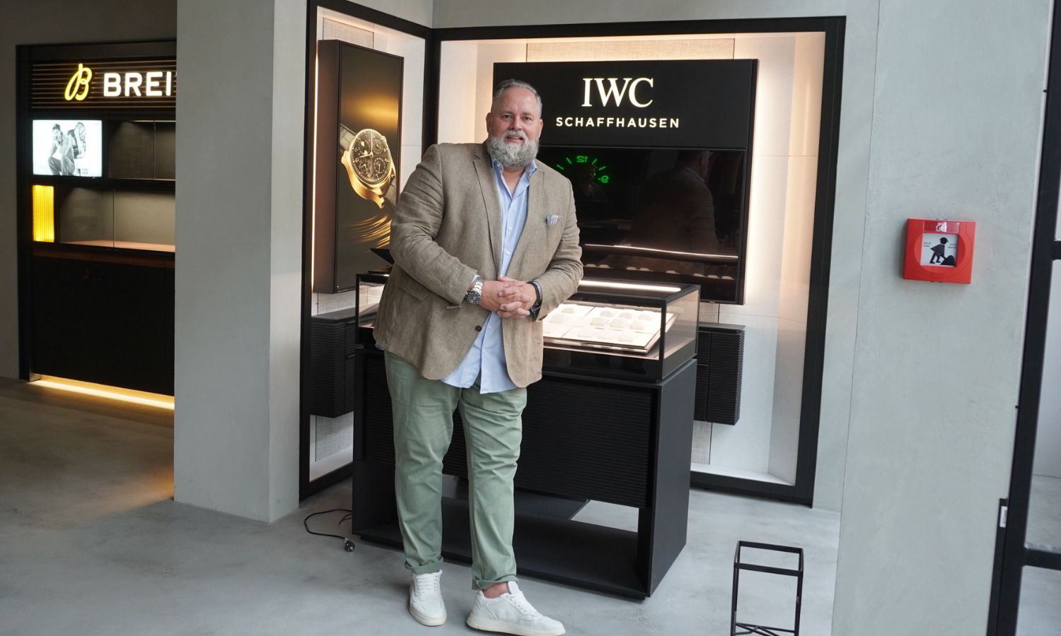 Patrick Weerts mit blauem Hemd, beigem Jackett und grüner Chino bei ALTHERR in Hannover vor dem Hintergrund der Marken IWC und Breitling
