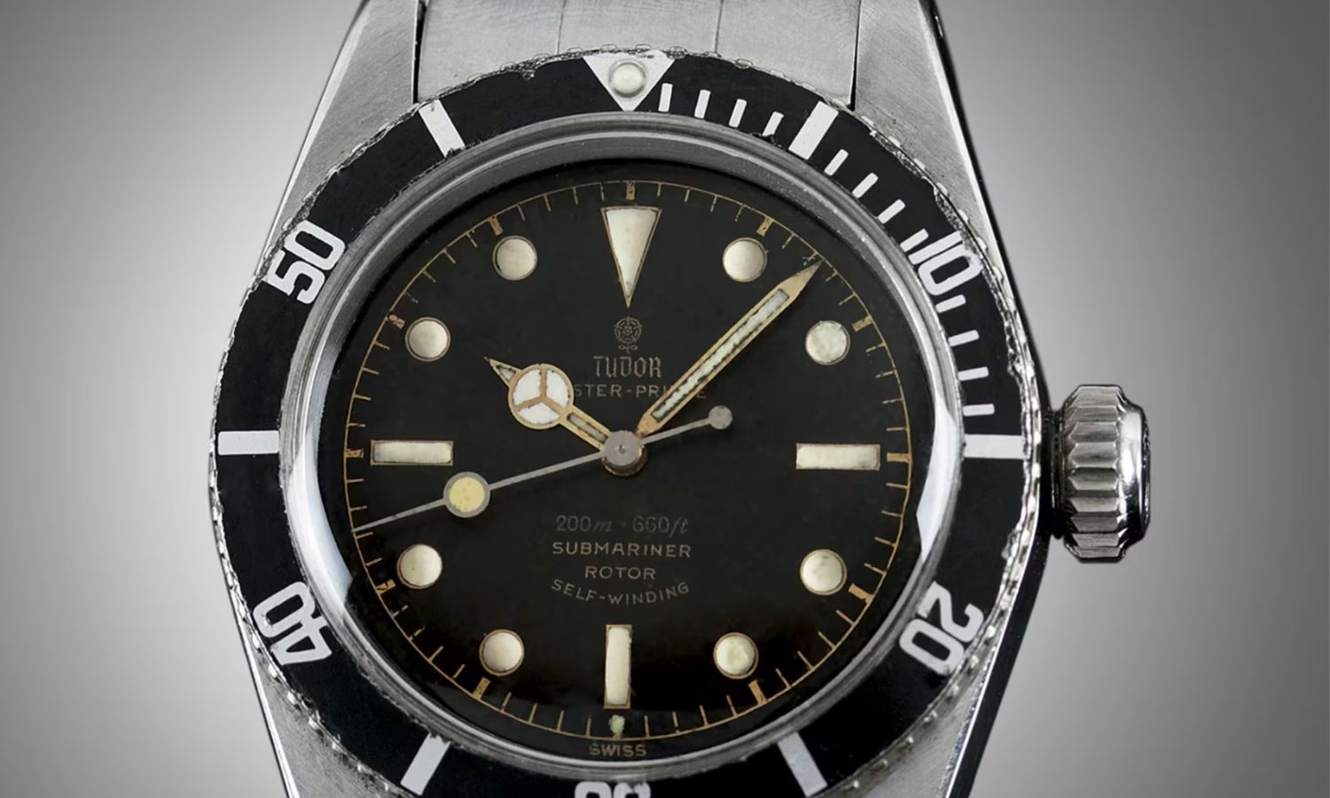 TUDOR Big Crown aus 1958 mit schwarzem Zifferblatt, schwarzer Lünette und Edelstahlarmband vor grauem Hintergrund
