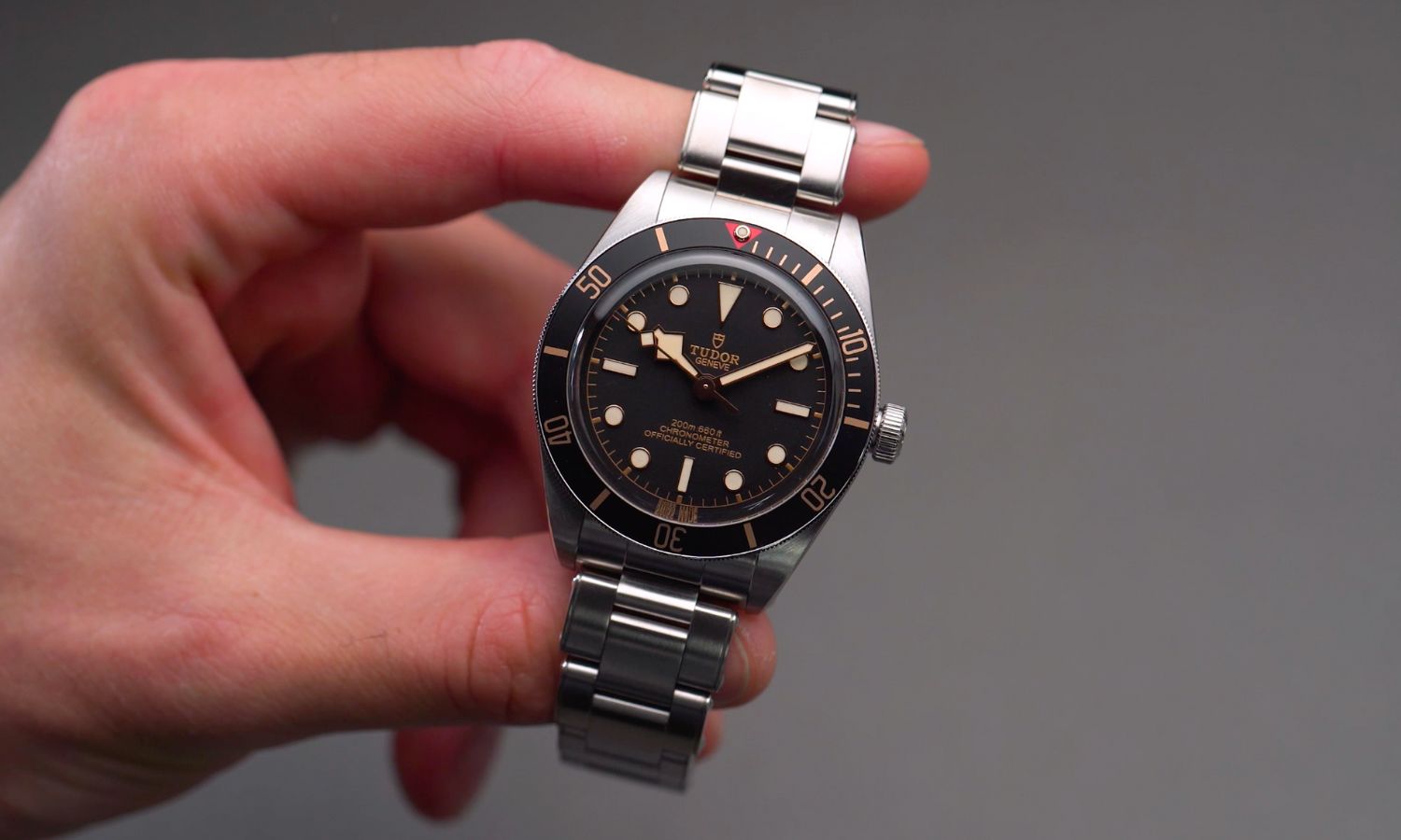 TUDOR Black Bay 58 Referenz M79030N-0001 mit schwarzem Zifferblatt und schwarzer Lünette am Edelstahlarmband in einer Hand gehalten vor grauem Hintergrund