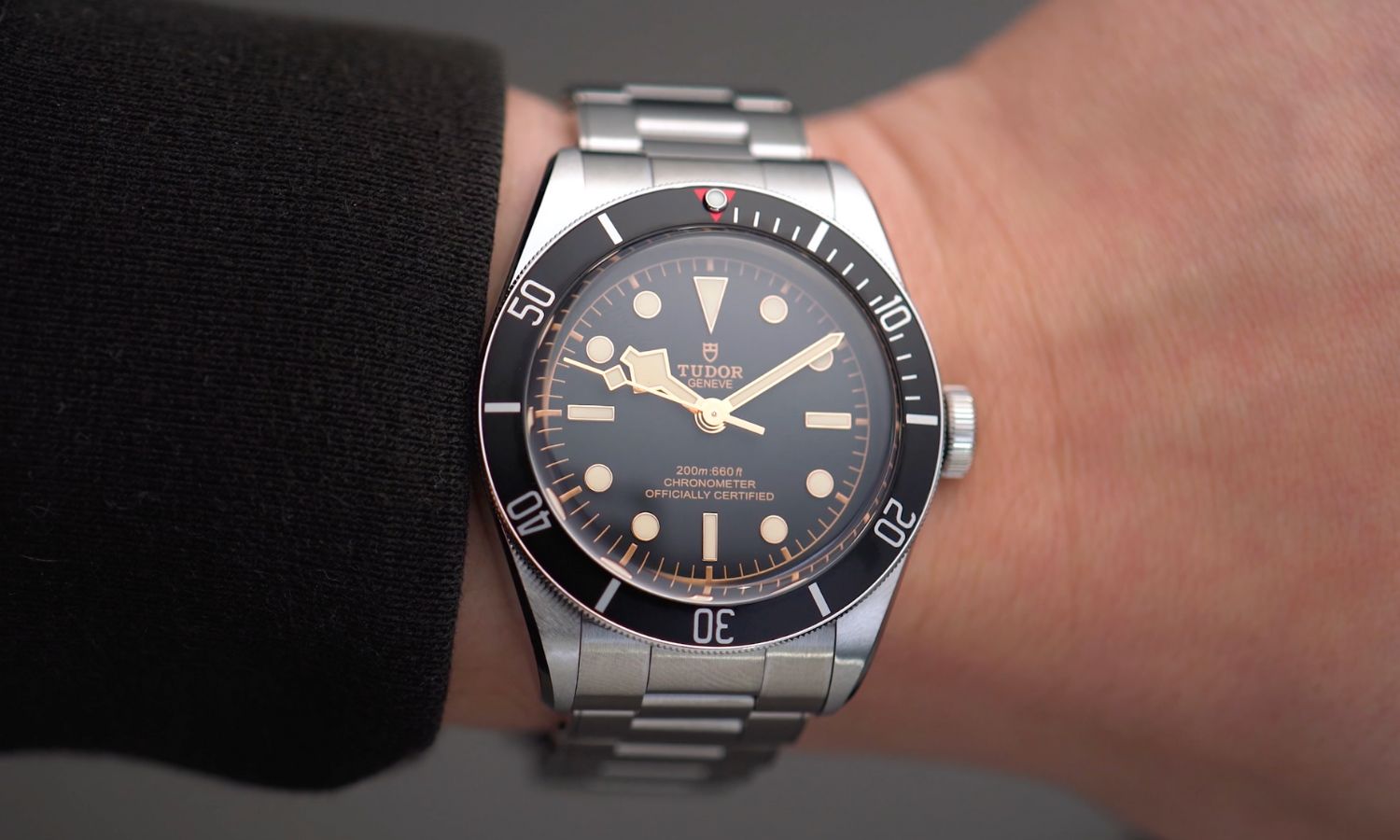 TUDOR Black Bay 58 Referenz M79030N-0001 mit schwarzem Zifferblatt und schwarzer Lünette am Edelstahlarmband an einem Handgelenk mit schwarzem Ärmel getragen vor grauem Hintergrund