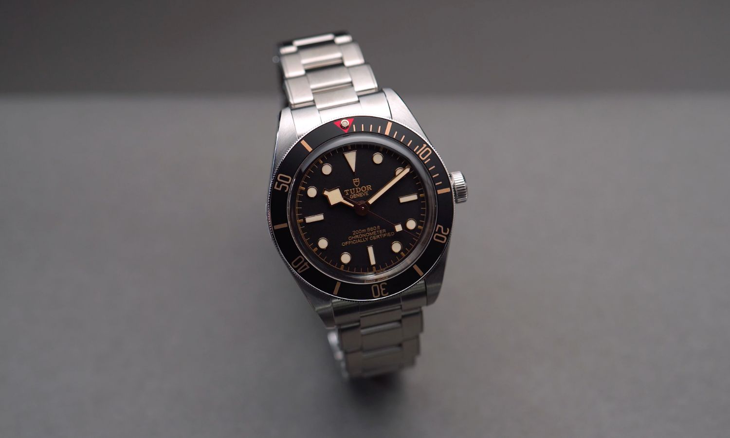 TUDOR Black Bay 58 Referenz M79030N-0001 mit schwarzem Zifferblatt und schwarzer Lünette am Edelstahlarmband stehend vor grauem Hintergrund