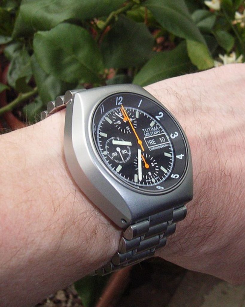 Tutima Fliegerchrono mit schwarzem Zifferblatt abgebildet an einem Handgelenk vor grünem Naturhintergrund