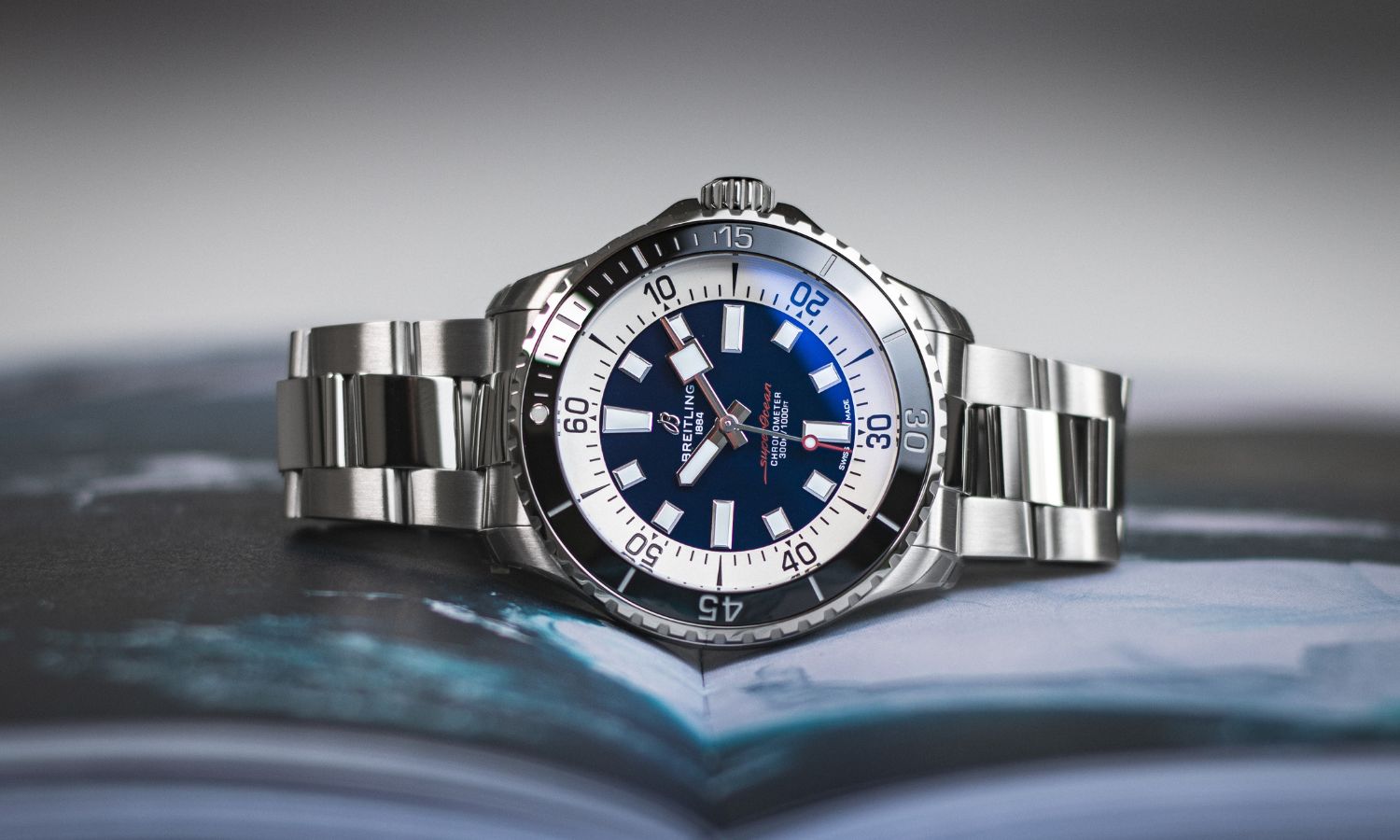 Breitling Superocean Automatic 44 mit blauem Zifferblatt am Edelstahlarmband auf der Seite liegend vor grauem Hintergrund