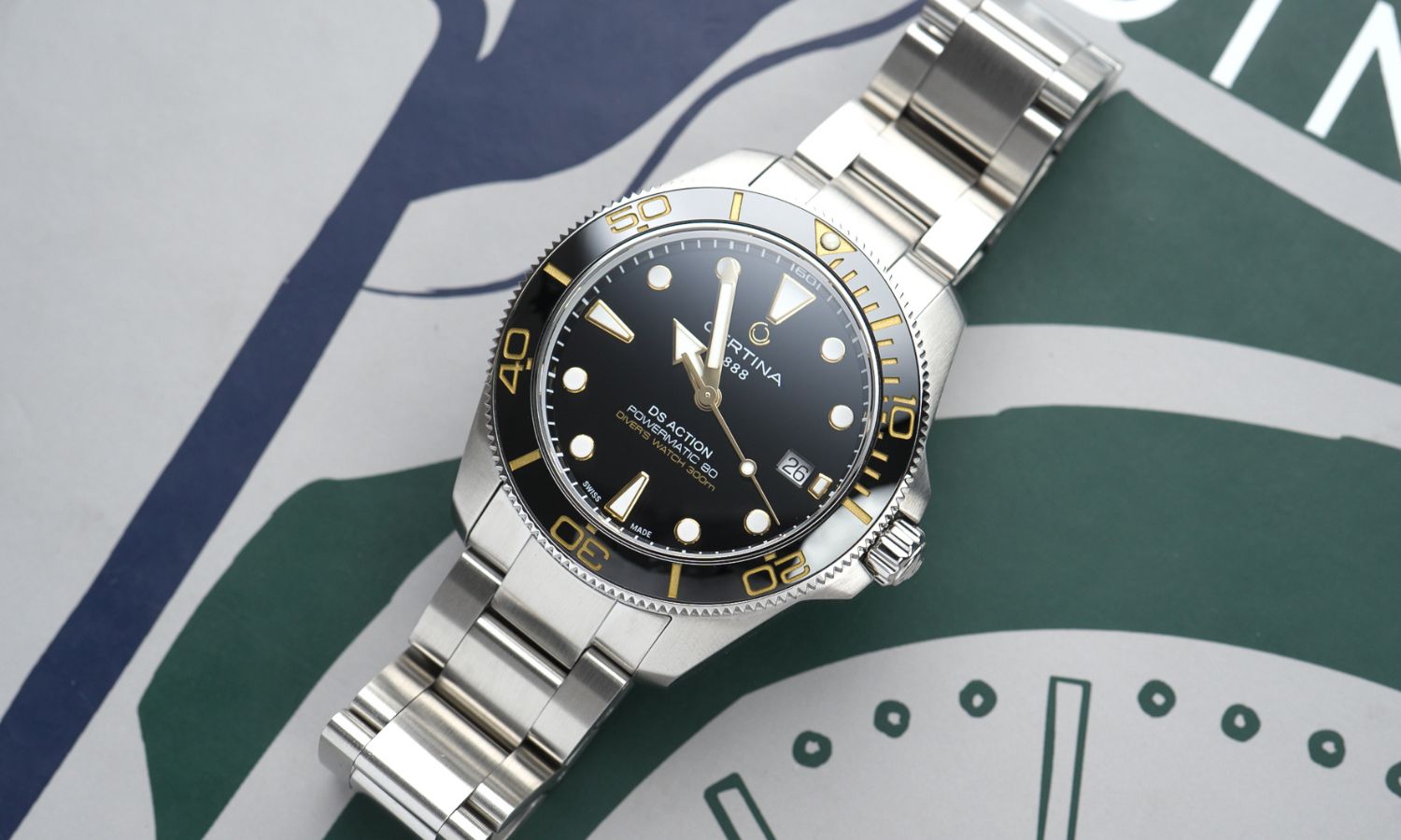 Certina DS Action Diver 40,5mm Powermatic 80 Referenz: C048.407.11.051.01 mit schwarzem Zifferblatt am Edelstahlarmband liegend vor dunkelgrünem Hintergrund mit weißen Mustern