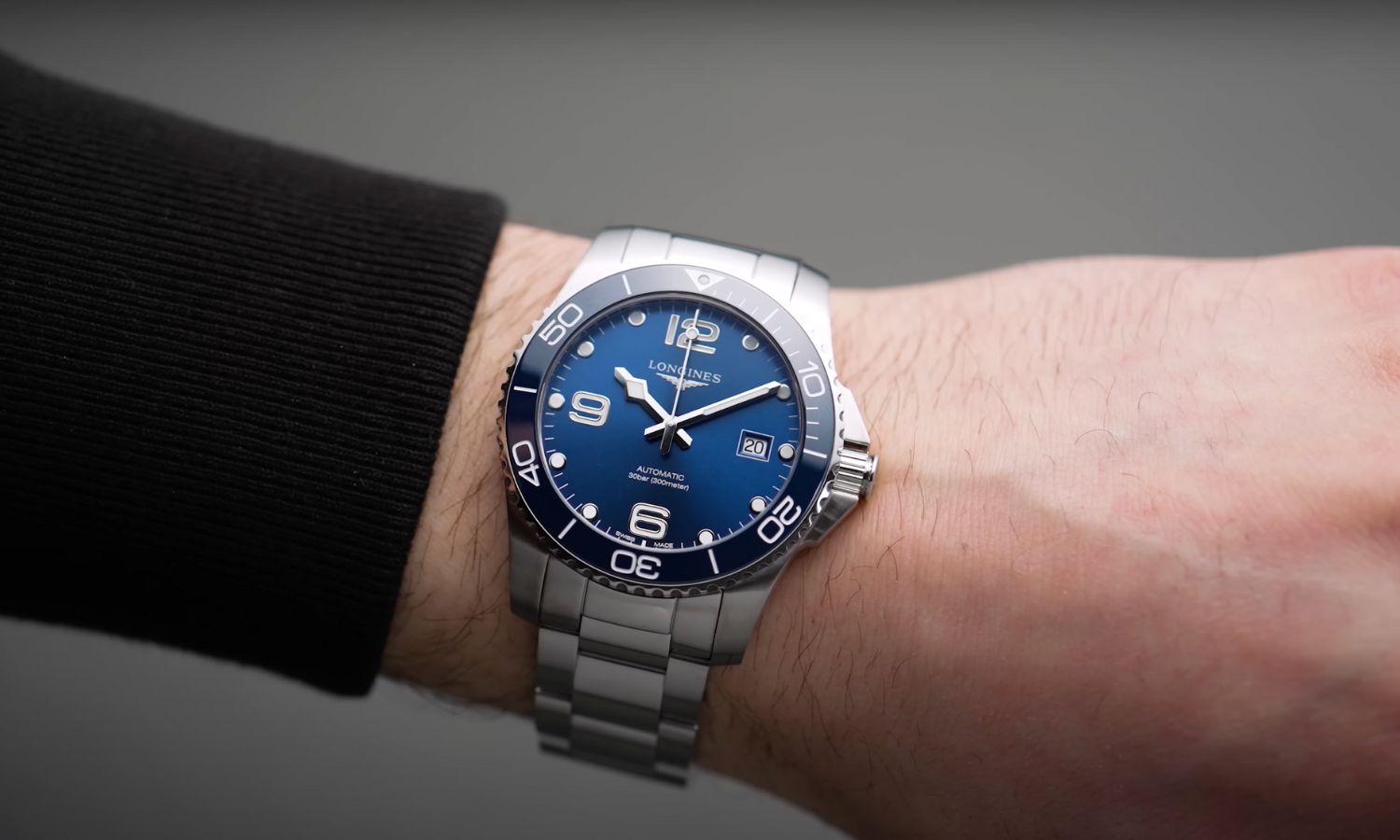 Longines HydroConquest 41 mit blauem Zifferblatt am Edelstahlarmband an einem Handgelenk mit schwarzem Ärmel getragen vor grauem Hintergrund