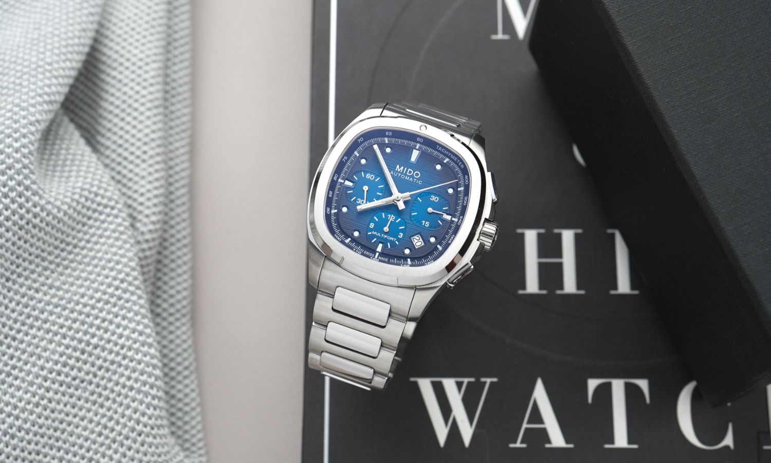 Mido Multifort TV Chronograph Referenz: M049.527.11.041.00 mit blauem Zifferblatt am Edelstahlarmband stehend auf einem schwarzen Buch mit weißen Schriftzügen
