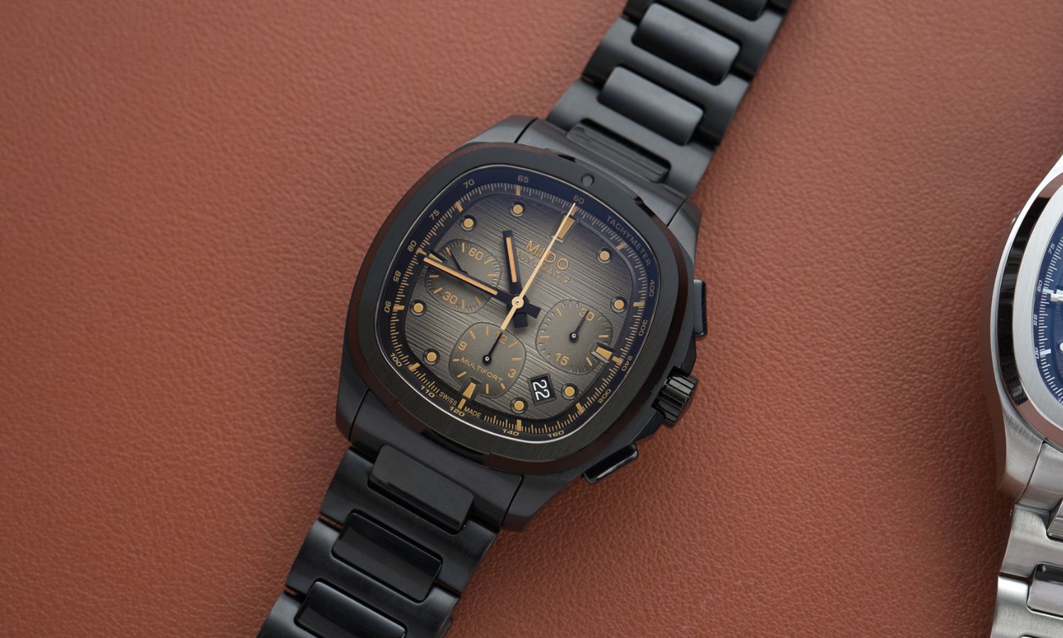 Mido Multifort TV Chronograph Referenz: M049.527.33.081.00 mit schwarzem Zifferblatt am schwarzen Edelstahlarmband liegend vor braunem Hintergrund